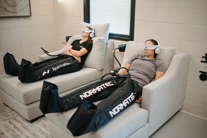 Two clients relaxing in recliners during a Normatec compression therapy session